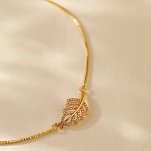 Macro shot of gold box chain bracelet with leaf-shaped pendant inlaid with white zircon