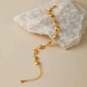 Detail of bohemian heart-shaped link bracelet with 18K gold finish and amber enamel