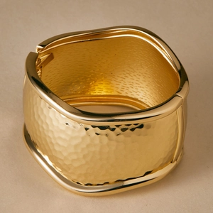Close-up of golden wide cuff bracelet featuring hammered texture and a side hinge