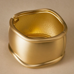 Macro detail of wide gold alloy bracelet featuring matte exterior and glossy interior textures