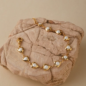 Detail of 18K gold-plated heart bracelet with pearl inlay on natural stone background
