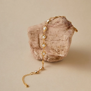 Detail of 18K gold-plated heart-shaped pearl bracelet draped on natural stone