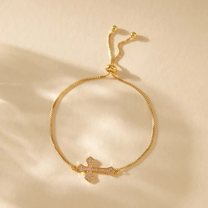 Close-up of gold-plated box chain bracelet with sparkling cross pendant and slider buckle