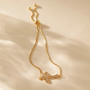 Detailed close-up of a gold cross bracelet with shimmering crystals and adjustable slider