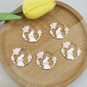 Set of five gold-rimmed white rabbit charms with pink flowers on a wooden tray
