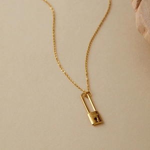 Collana in acciaio inossidabile dorato con ciondolo a lucchetto inciso Love su sfondo beige