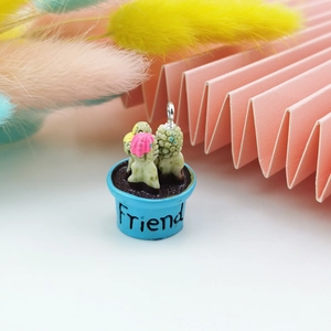 Dettaglio di un ciondolo a forma di cactus in resina con scritta Friend e vaso blu