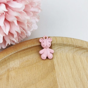 Close-up of a pink matte teddy bear DIY pendant on a wooden tray with flowers