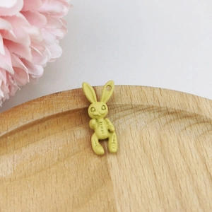 Close-up of matte yellow bunny pendant with stitching detail on a wooden tray