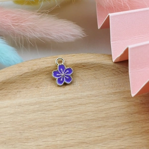 Detail of purple five-petal flower charm with gold trim on a wooden tray for DIY jewelry