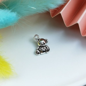 Detail of silver bear charm with bow for DIY jewelry making on soft feather background