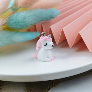 Detailed view of 3D resin unicorn pendant charm with pink feathers background