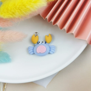 Gros plan d'une breloque crabe en résine bleue et rose avec anneau argenté sur assiette