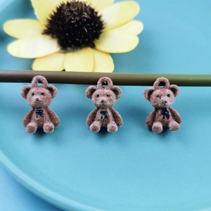 Three brown flocked bear charms with black bows on a ceramic plate for DIY jewelry making