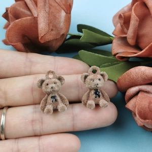Close-up of brown flocked bear pendant on a fingertip showing its small size and texture