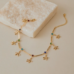 Gros plan sur un bracelet de cheville doré avec pendentifs étoile de mer et cristaux