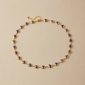 Detailed macro view of vintage gold heart necklace with blue enamel on flat background