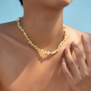 Halskette mit unregelmäßigen weißen Kristallen und Goldperlen am Model vor blauem Himmel