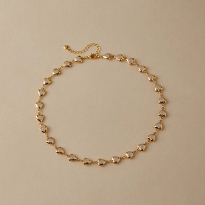 Detail view of a gold heart-shaped choker featuring white inlay accents and lobster clasp