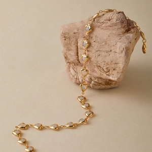 Detail of heart-shaped gold necklace with iridescent stone inlays on textured stone