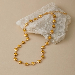 Macro detail of 18K gold plated heart link necklace on a white mineral stone background