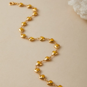 Close-up of golden heart chain bracelet with amber resin inlays on textured background