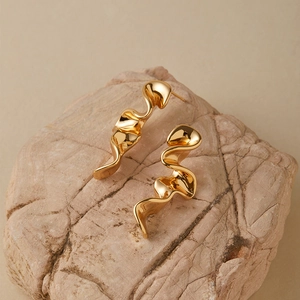 Polished gold irregular wavy drop earrings displayed on a natural stone base