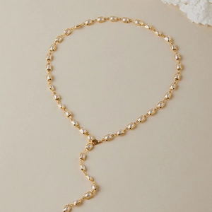 Détail du collier en Y plaqué or avec perles rectangulaires sur fond beige chaleureux