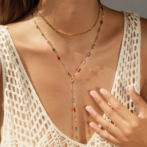 Détail d'un collier doré multicouche avec gemmes colorées sur un tissu en dentelle