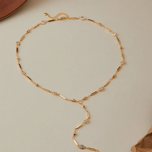 Golden Y-shaped necklace with rectangular bars and zircon stones on a beige backdrop