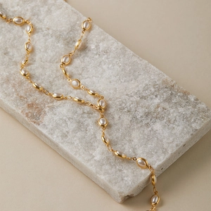 Détail du collier doré multicouche avec charmes ovales en perles blanches sur marbre