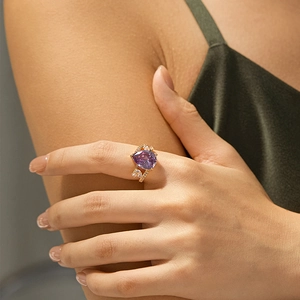 Macro detail of 18K gold ring with purple pear-cut stone and heart accents on finger