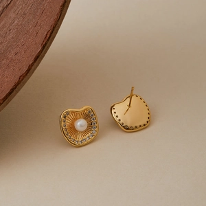 Boucles d'oreilles dorées irrégulières avec perle et zircons sur fond beige