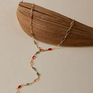 Détail d'une chaîne de corps en Y dorée avec des gemmes marquises colorées sur une feuille