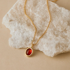 Elegant gold necklace with oval red gemstone pendant displayed on a natural white rock