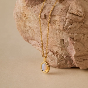 Close-up of gold cross chain necklace with iridescent opal pendant on natural stone