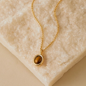Macro shot of gold necklace featuring oval tiger eye stone pendant on crystal stone