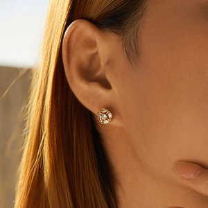 Close-up of golden floral stud earring with marquise crystals on female ear model
