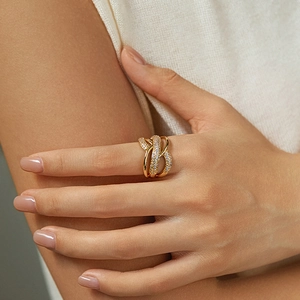 Close-up of a layered gold ring with zircons on a model's finger with a soft fabric background
