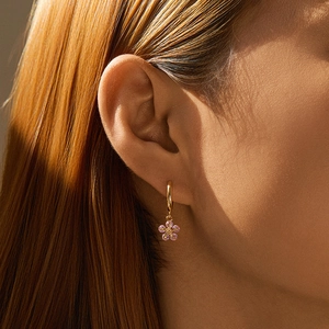 Detail von goldenen Creolen mit rosa Zirkonia-Blütenanhänger am Ohr eines Modells