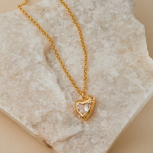 Macro shot of vintage gold heart pendant with textured metal and clear zircon on stone