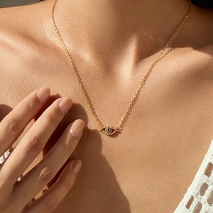 Detail of 18K gold plated evil eye pendant necklace with crystals on a woman's collarbone