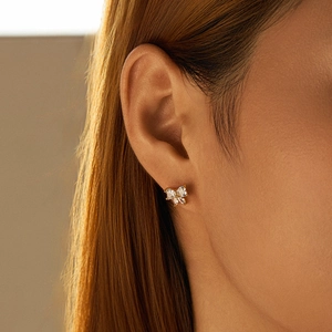 Macro shot of small gold bow stud earrings with sparkling crystals on model ear