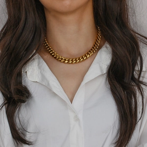 Close-up of a bold gold Cuban link necklace worn with a clean white minimalist shirt