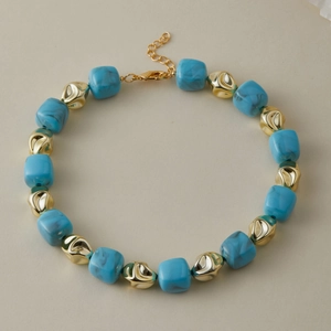 Dettaglio della collana con cubi in resina blu marmorizzata e perle dorate irregolari