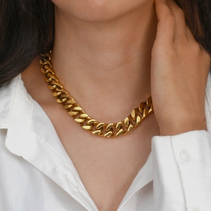 Close-up of a chunky gold Cuban link chain necklace worn over a white shirt