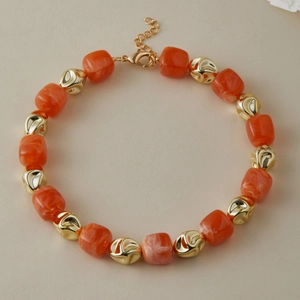 Dettaglio di grandi perle di resina marmorizzata arancione con accenti metallici dorati