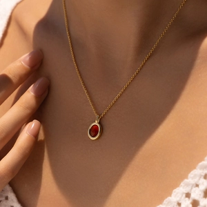 Close-up of a 18K gold-plated necklace featuring an oval red gemstone on a woman's collarbone