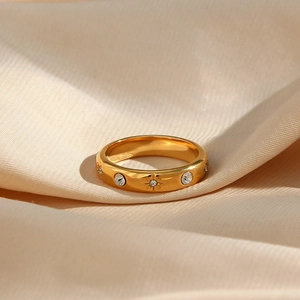 Dettaglio anello in acciaio placcato oro 18K con zirconi su sfondo di tessuto satin