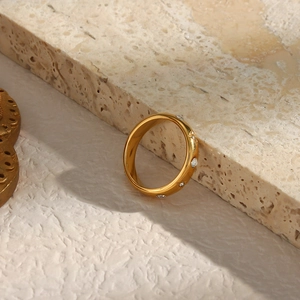 Dettaglio anello in acciaio inossidabile placcato oro 18K con zirconi su sfondo pietra